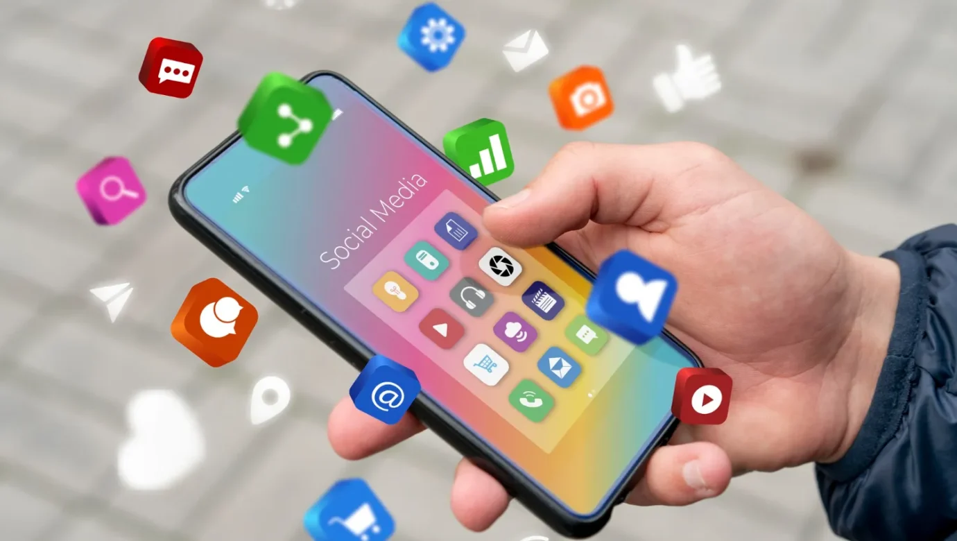 Un usuario sostiene un teléfono inteligente con íconos de aplicaciones de redes sociales flotando alrededor, representando la interacción digital y la conectividad en línea.